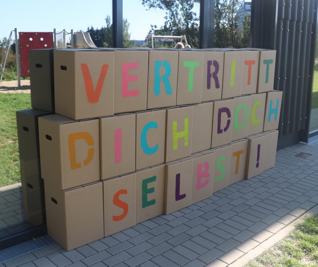 Auf jedem Karton steht ein Buchstabe. Zusammen ergeben sie: Vertritt dich doch selbst!
